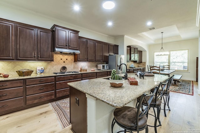 kitchen with pendant lighting, stainless steel appliances, a raised ceiling, and an island with sink