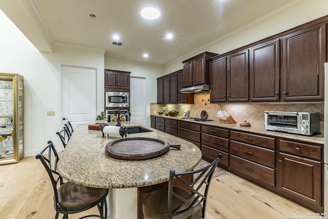 kitchen featuring sink, a kitchen island with sink, dark brown cabinets, stainless steel appliances, and light stone countertops