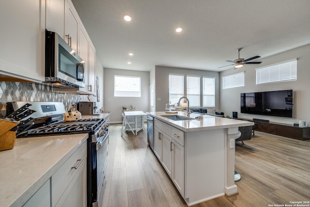 kitchen featuring backsplash, appliances with stainless steel finishes, an island with sink, white cabinets, and light wood-type flooring