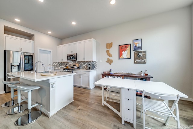 kitchen with decorative backsplash, an island with sink, a kitchen bar, white cabinetry, and stainless steel appliances