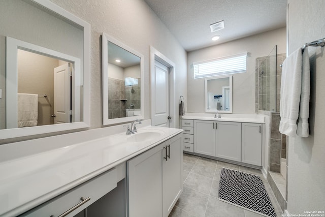 bathroom with a tile shower, tile patterned flooring, vanity, and a textured ceiling