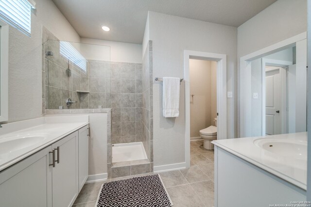 bathroom with tiled shower, tile patterned flooring, vanity, and toilet