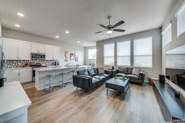 living room featuring a textured ceiling, light hardwood / wood-style floors, and ceiling fan