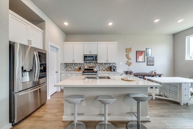 kitchen with white cabinetry, a kitchen island with sink, a kitchen breakfast bar, and appliances with stainless steel finishes