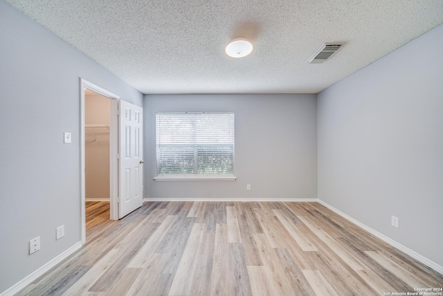 unfurnished room with a textured ceiling and light hardwood / wood-style floors