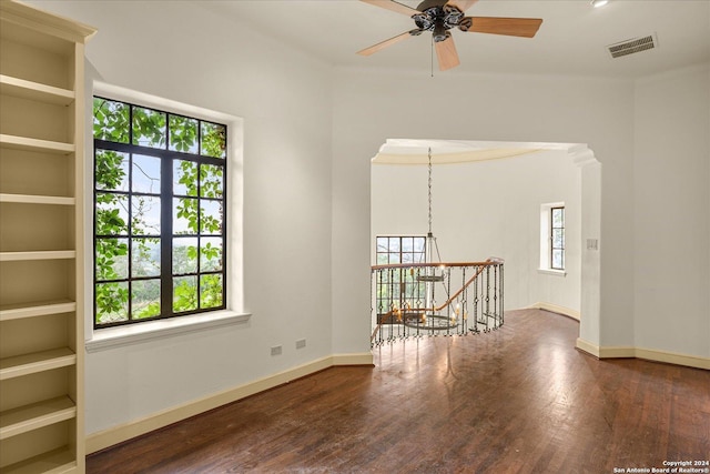 spare room featuring dark wood-type flooring, plenty of natural light, and ceiling fan with notable chandelier