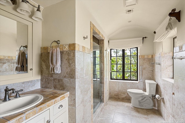 bathroom with toilet, tile walls, vanity, a shower with door, and tile patterned flooring