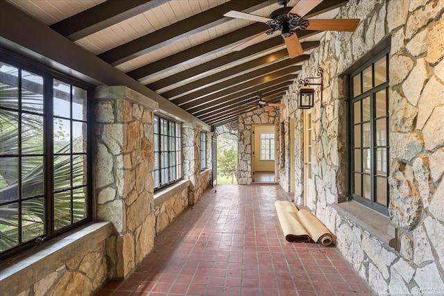 unfurnished sunroom with a healthy amount of sunlight, vaulted ceiling with beams, and ceiling fan