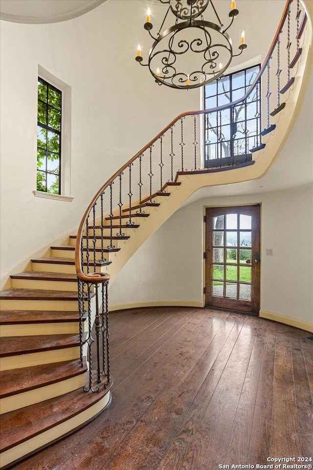 stairway with an inviting chandelier, a towering ceiling, and wood-type flooring