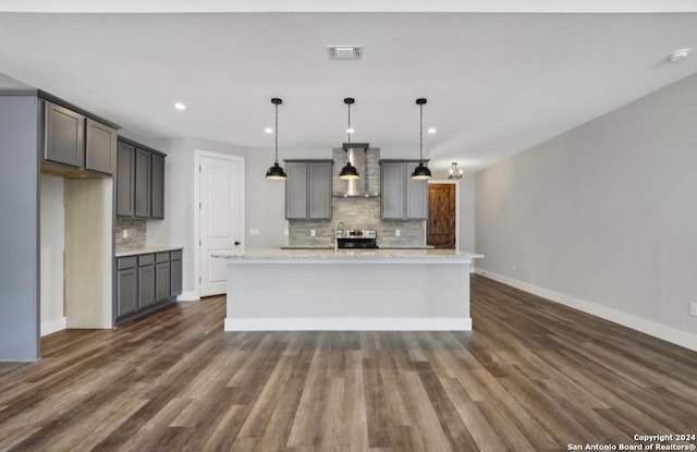 kitchen featuring gray cabinetry, hanging light fixtures, wall chimney range hood, backsplash, and a kitchen island with sink