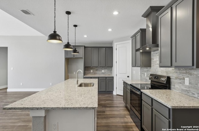 kitchen featuring sink, wall chimney exhaust hood, hanging light fixtures, black range with electric cooktop, and an island with sink