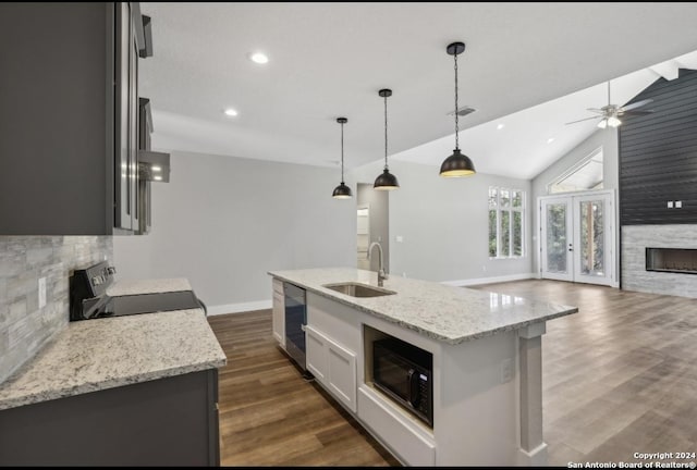 kitchen with black microwave, sink, stove, pendant lighting, and a kitchen island with sink