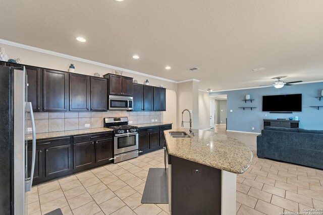 kitchen featuring appliances with stainless steel finishes, tasteful backsplash, ornamental molding, a kitchen island with sink, and sink