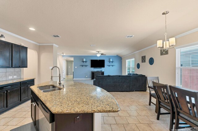 kitchen featuring sink, ornamental molding, an island with sink, tasteful backsplash, and decorative light fixtures