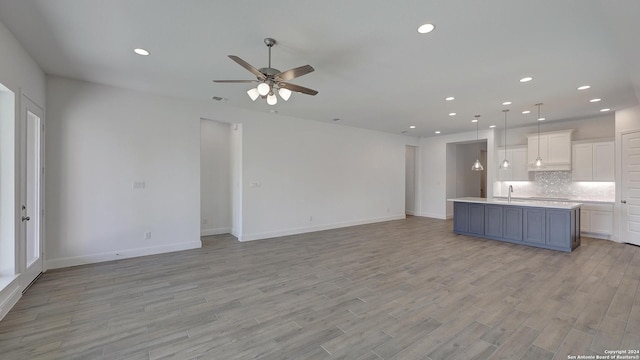 unfurnished living room featuring light wood-type flooring, ceiling fan, and sink