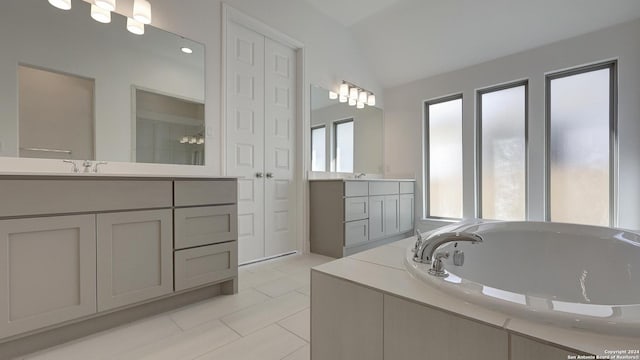 bathroom with tile patterned flooring, vanity, lofted ceiling, and tiled tub