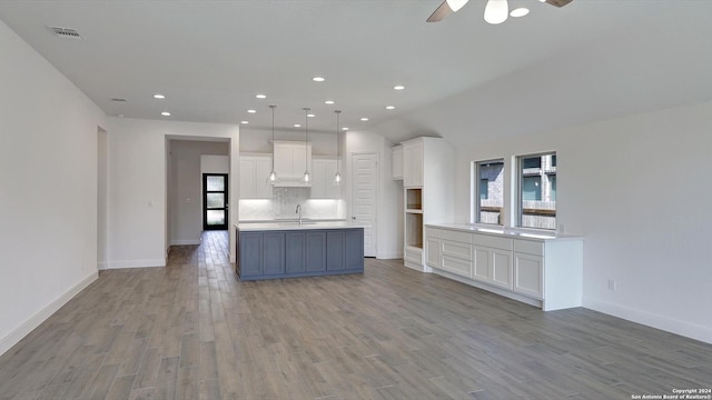 kitchen featuring backsplash, a center island with sink, ceiling fan, light hardwood / wood-style floors, and white cabinetry