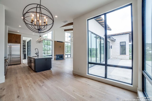 kitchen featuring built in refrigerator, a chandelier, light wood-type flooring, an island with sink, and pendant lighting