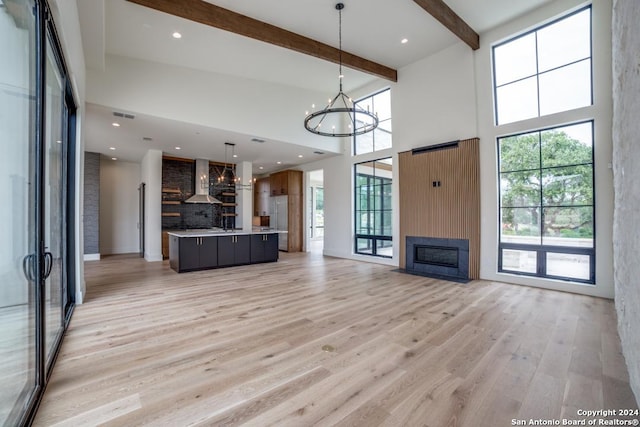 unfurnished living room featuring beam ceiling, a notable chandelier, a towering ceiling, a fireplace, and light hardwood / wood-style floors