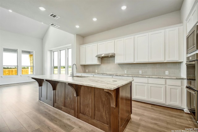 kitchen with lofted ceiling, a kitchen island with sink, sink, light stone countertops, and white cabinetry