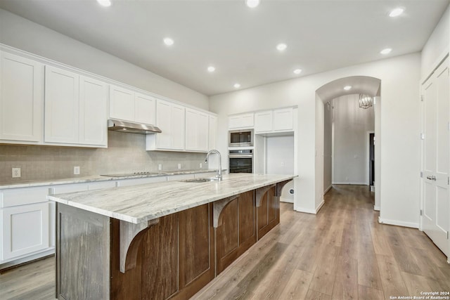 kitchen with stainless steel oven, a center island with sink, sink, built in microwave, and white cabinetry