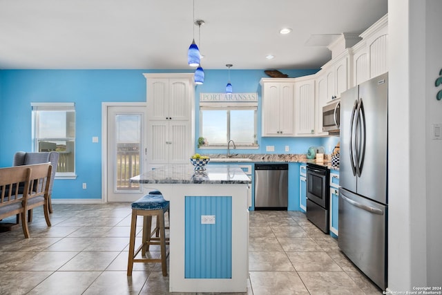 kitchen with a kitchen island, a wealth of natural light, decorative light fixtures, white cabinetry, and stainless steel appliances