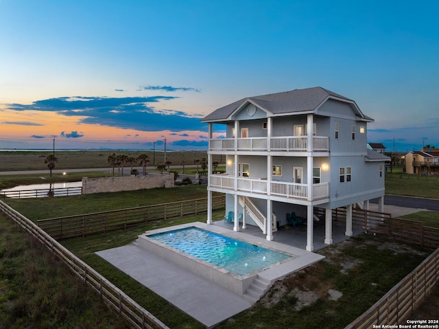 back house at dusk featuring a fenced in pool, a lawn, a patio, and a balcony