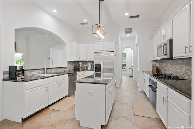 kitchen with white cabinets, appliances with stainless steel finishes, a center island, decorative light fixtures, and sink