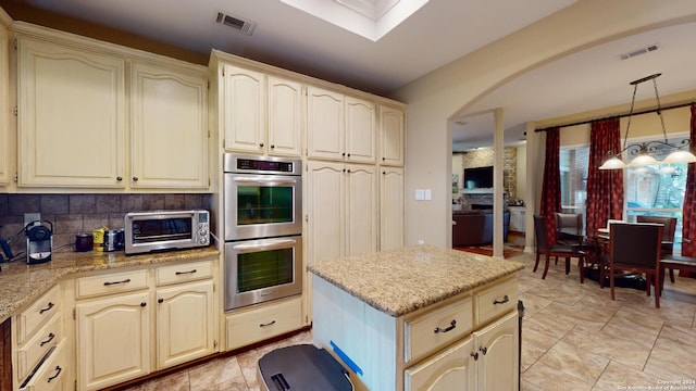 kitchen featuring pendant lighting, cream cabinets, light stone countertops, and double oven