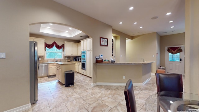 kitchen featuring sink, appliances with stainless steel finishes, a center island, decorative backsplash, and a raised ceiling