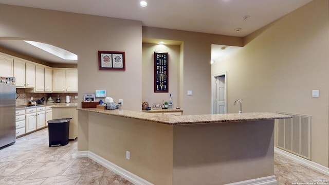 kitchen with stainless steel fridge, a center island, tasteful backsplash, light stone countertops, and kitchen peninsula