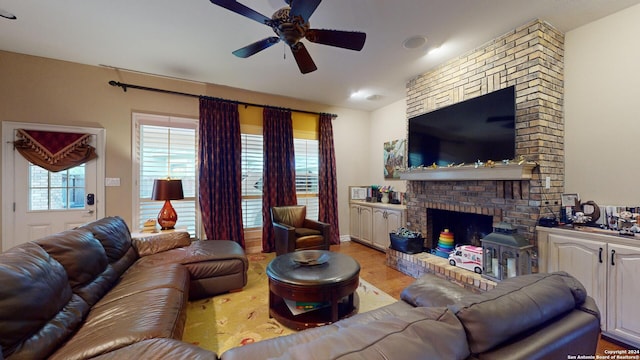 living room with ceiling fan, a brick fireplace, and light wood-type flooring