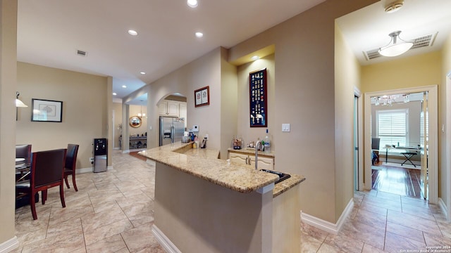 kitchen featuring stainless steel fridge, kitchen peninsula, and light stone countertops