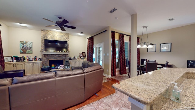 living room featuring ceiling fan with notable chandelier, a brick fireplace, and light wood-type flooring