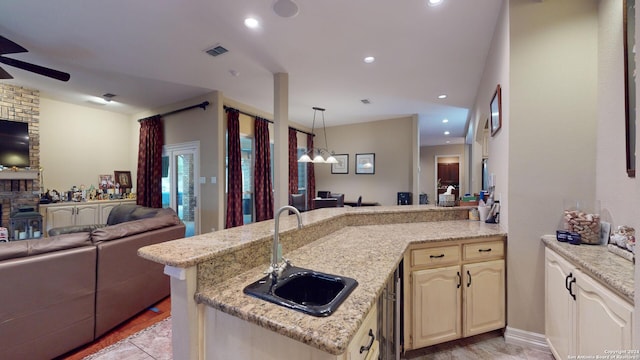 kitchen with sink, light stone counters, kitchen peninsula, ceiling fan, and a fireplace