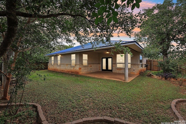 back house at dusk with a lawn and a patio