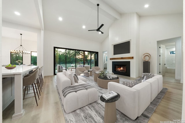 living room with beam ceiling, ceiling fan with notable chandelier, light hardwood / wood-style floors, and high vaulted ceiling