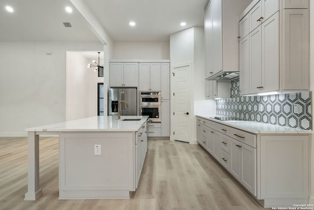 kitchen featuring backsplash, stainless steel appliances, a kitchen island with sink, light hardwood / wood-style flooring, and white cabinetry