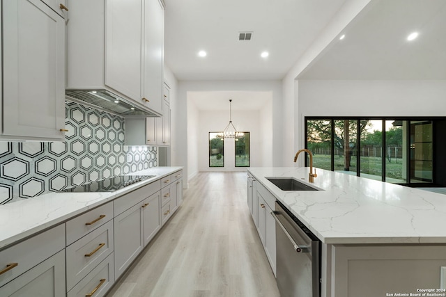 kitchen with light stone counters, electric stovetop, sink, dishwasher, and an island with sink