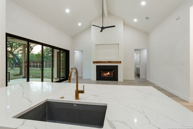 kitchen featuring light stone countertops, sink, high vaulted ceiling, light hardwood / wood-style floors, and a fireplace