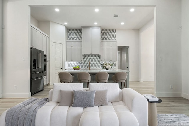 kitchen with a kitchen island with sink, high end refrigerator, decorative backsplash, light hardwood / wood-style floors, and a breakfast bar area