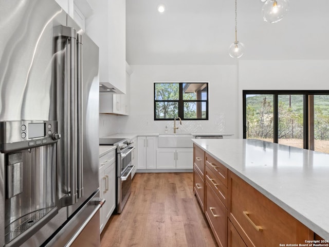 kitchen with white cabinetry, sink, light hardwood / wood-style floors, pendant lighting, and appliances with stainless steel finishes