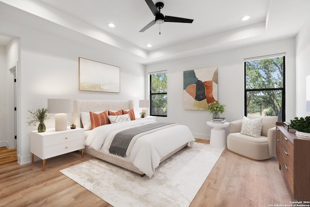 bedroom with ceiling fan, a raised ceiling, and light wood-type flooring