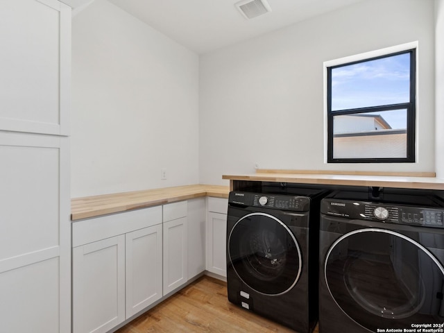 laundry area featuring cabinets, light hardwood / wood-style flooring, and washer and clothes dryer