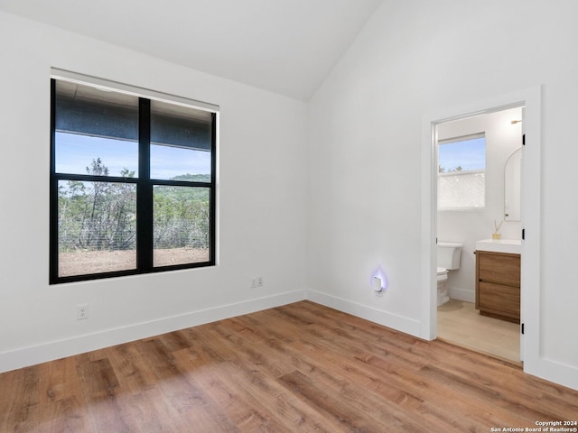 unfurnished bedroom featuring ensuite bathroom, light hardwood / wood-style flooring, and lofted ceiling