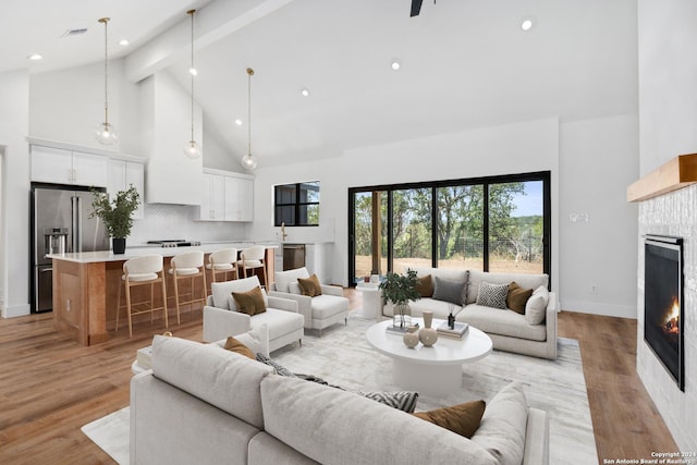 living room featuring a tiled fireplace, beamed ceiling, high vaulted ceiling, and light wood-type flooring