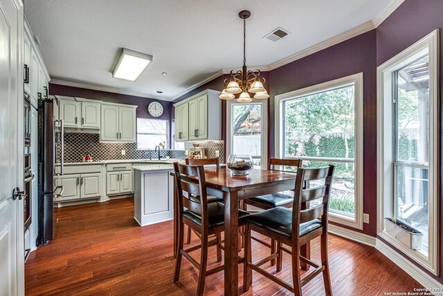 dining area featuring sink, crown molding, dark wood-type flooring, an inviting chandelier, and plenty of natural light