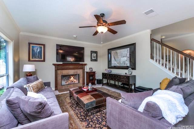 living room featuring a tiled fireplace, crown molding, and ceiling fan