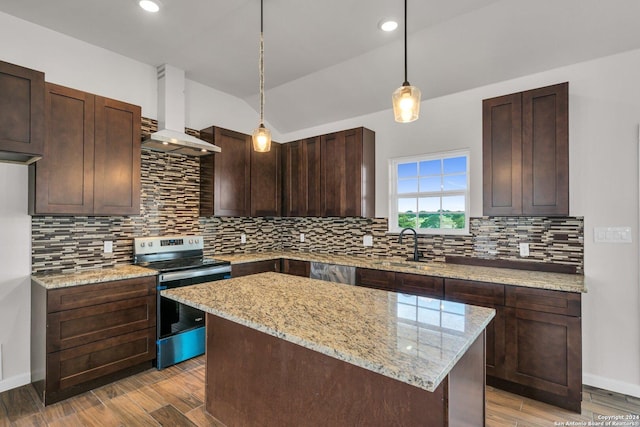 kitchen with electric stove, wall chimney range hood, pendant lighting, light stone counters, and a kitchen island