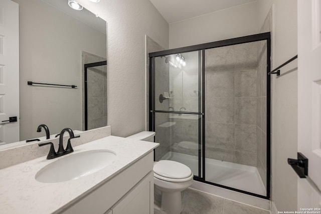 bathroom with tile patterned flooring, vanity, a shower with shower door, and toilet